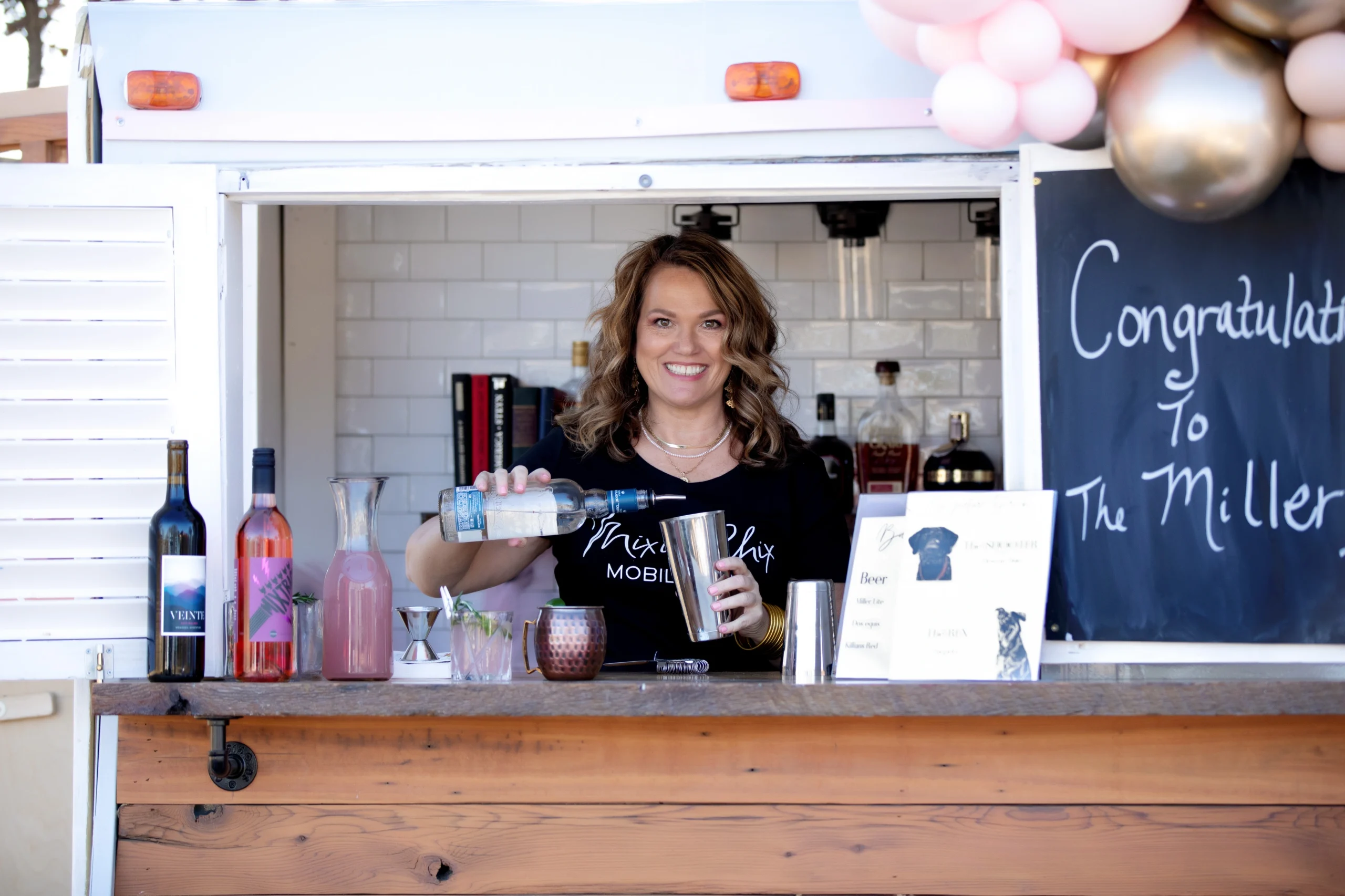 Rachel O’Brien, co-owner of Mixie Chix Mobile Bar, serving craft cocktails from the vintage trailer bar at an event in Fort Worth, Texas.